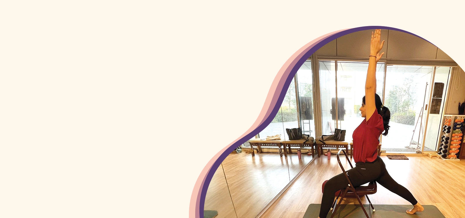 Woman practicing chair yoga with arms extended upward in a mirrored studio space